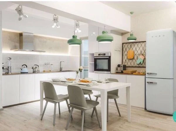 White kitchen cabinetry beside a dining table and green pendant lights